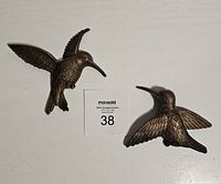 Two bronze-tone plastic hummingbird wall decorations displayed on a white floor with a auction lot card labeled 38 between them.