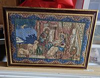 Full view of framed needlepoint showing Nativity scene with Mary, Joseph, Baby Jesus, and animals against a blue starry sky bordered by a decorative pattern.