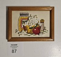 Frontal photo of vintage framed popcorn crewel embroidery depicting popcorn jar, bowl, apple, and salt shaker.