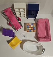 Photo showing the full set of doll furniture items including pink lounge chair, white shelving unit, blue cabinet, tiled table, pink sofa, yellow chair, purple chair, and white bathtub, all arranged on a white surface.