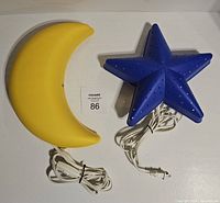 Top view of yellow crescent moon and blue star Ikea wall lamps with attached cords and plugs, showing front design.