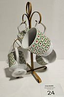 Four Levco stacking mugs arranged on the vintage gold-tone metal mug rack, showing the geometric green and red pattern on white ceramic mugs and the rack's elegant curved design.