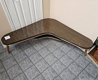 Boosterang shaped mid-century modern coffee table with woodgrain Formica top and lower shelf, shown from front right angle.