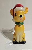 Front view of yellow and white deer fawn blow mold with big eyes, black nose, red Santa hat with white trim and green collar with gold bell.