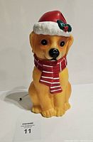 Front view of golden retriever blow mold wearing red Santa hat and red and white striped scarf, depicting facial details and sitting pose.