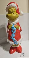 Front view of the Grinch blow mold figure with a mischievous expression, dressed in Santa red and white outfit holding a blue polka dot stocking.