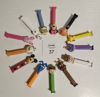 Top-down photo showing all 14 PEZ dispensers arranged in a circle around a card with lot number 37. Characters include various themed and colored heads, predominantly animals and cartoons.