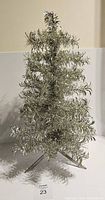 Front view of silver tinsel Christmas tree showing the pom pom style branches and metal stand with three legs, standing upright but missing a support part.