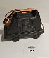 Side view of the black hard plastic Star Wars droid shaped shoulder bag with a brown faux leather shoulder strap laid across the front.