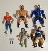 Front view of five vintage action figures: muscular bearded figure, blue star helmet figure, red shirt figure, masked figure with white pants, and armored figure.