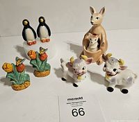 Four vintage ceramic salt and pepper shakers: pair of penguins, kangaroo with baby, pair of cows, and pair of tulip flowers with bees, displayed on white surface with auction card.