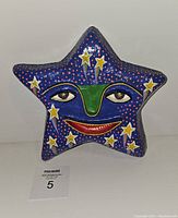 Front view of vintage paper mache star mask with blue background and yellow stars, showing a face with green nose, yellow eyes, and red mouth.