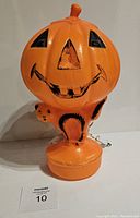 Front view of the vintage blow mold showing the pumpkin with a smiling jack-o-lantern face, sitting on a black cat figure. The front face shows paint loss on the pumpkin face details, orange and black paint on cat is intact.
