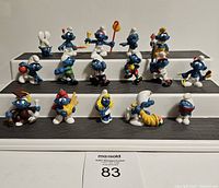 Front view of 18 vintage Smurf figures arranged on stepped display stand showing various characters and colors.