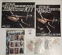 Photo showing the Star Wars Postage Stamp Collecting Kit, Star Wars Stamp Album, a full sheet of $2.00 Star Wars character stamps, and several smaller bags containing multiple loose stamps.