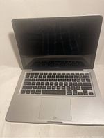 Full view of opened Apple MacBook showing keyboard, screen, and trackpad with visible crack