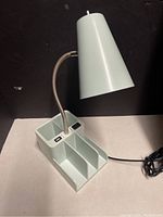 Desk lamp with conical shade and organizer base shown against a black background.