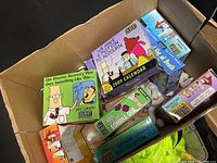 Photo showing a cardboard box filled with various Dilbert-themed calendars including yearly wall calendars and smaller boxed calendars with colorful comic designs.