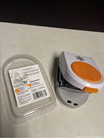 Photo showing front side of the Fiskars paper punch with orange lever and white plastic body, snowflake design on top.