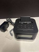 Front side view of black iHome dock clock showing digital screen and control buttons with plugged in power adapter cable visible.