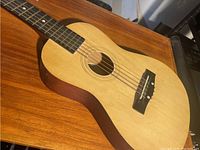 Full view of the kid's acoustic guitar showing the body with light wood top and darker sides and back, six strings, and bridge.