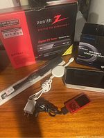 Photo showing Zenith TV tuner box, Samsung wireless charger box, Apple dock, Sony media player, cables, and red mp3 player on wooden surface.