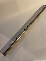 Full view of the metal flute showing the finger holes and overall shape and size.