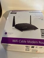 Photo of the original boxed black Netgear WiFi Cable Modem Router AC1200 with antennas, showing front of the box.