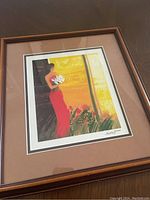 Framed artwork showing a woman in a red dress holding white flowers in an abstract flowery background.