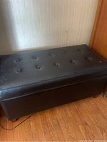 Black upholstered storage ottoman from a side angle showing button tufting and minor blemishes.