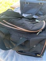 Black soft-sided pet carrier bag showing side mesh and zipper detail with carry straps and light wear marks.