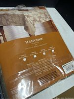 Photo of Harvest Season Leaf Solid Woven oblong tablecloth packaging showing beige leaf design and product details.