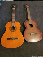 Both acoustic guitars side by side; one in natural wood finish, one in worn red finish.