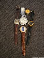Top-down image showing the 5 Fossil watches arranged on a dark carpeted surface to display strap and dial variety.