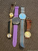All five Fossil watches laid on fabric surface showing straps and dials.