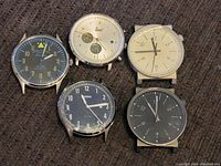 Image showing all 5 Fossil watch faces without bands, laid out on a dark textured fabric surface.