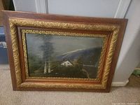 Framed oil landscape painting leaning against a wall showing entire artwork and frame.