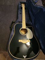Overhead shot of black acoustic-electric guitar in open hardshell case showing body, top, rosette and pickguard