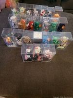 Overview photo of approximately 23 Ty Beanie Babies inside individual clear plastic display cases arranged on a surface.