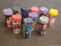 Photo showing 10 sealed Selena-themed tumblers on beige carpet, variety of lid colors and designs visible