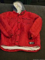 Full view of red puffy quilted jacket with hood and fleece lining, showing front pockets and elastic cuffs.