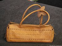 Full side view of tan leather purse showing cross-stitch decorative pattern and braided handles