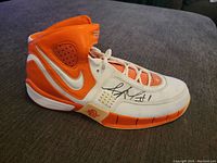 Side angle of the orange and white Nike Elite sneaker showing the autograph on the side.