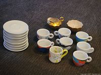 Full group of 8 colorful cups, 10 white saucers, gold-tone pitcher and bowl on dark fabric background