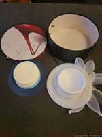 Two vintage women's hats lying next to an open round hat box with a red stiletto shoe design on the lid.