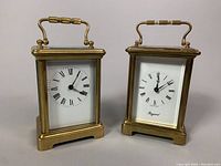 Front view of both brass carriage clocks showing the clock faces with Roman numerals and Bayard branding on one clock.