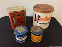 Group photo of four vintage covered tins: large white orange potato chip tin, red decorative tin, and two tobacco tins Philip Morris and Buckingham Fine Cut