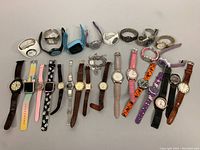 Photo showing 23 assorted wristwatches arranged in rows revealing variety of colors, styles, and strap materials.