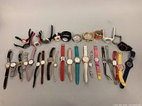 A top-down image showing twenty assorted wristwatches laid out in two rows. The watches vary in colors, bands, and styles including leather, metal, and synthetic straps.
