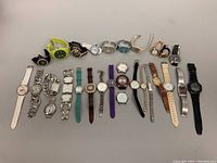 Top-down photo of 22 assorted watches laid out in rows, showing variety of band materials, colors, and watch face styles.